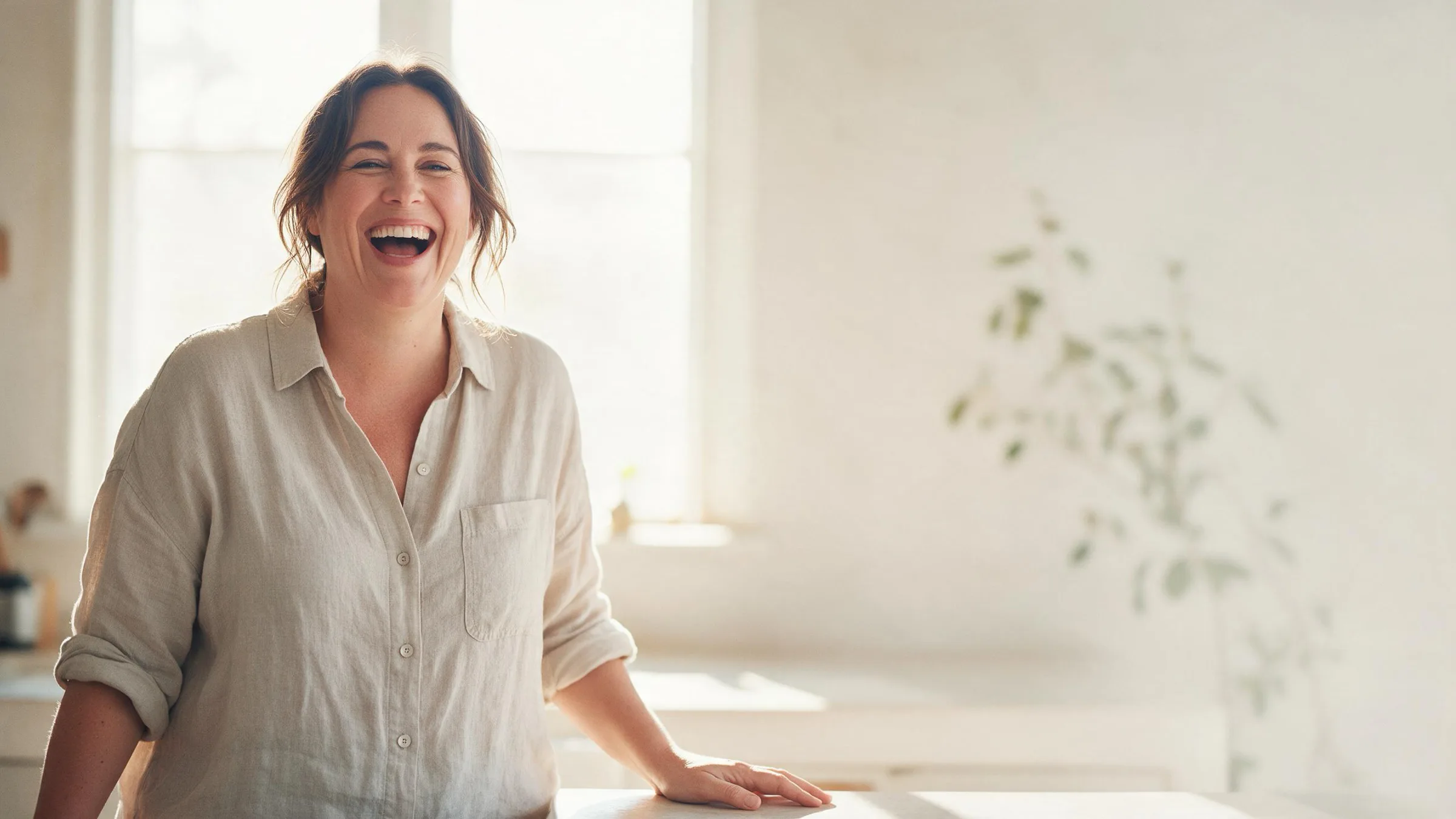 A woman laughing in a sunlit kitchen
