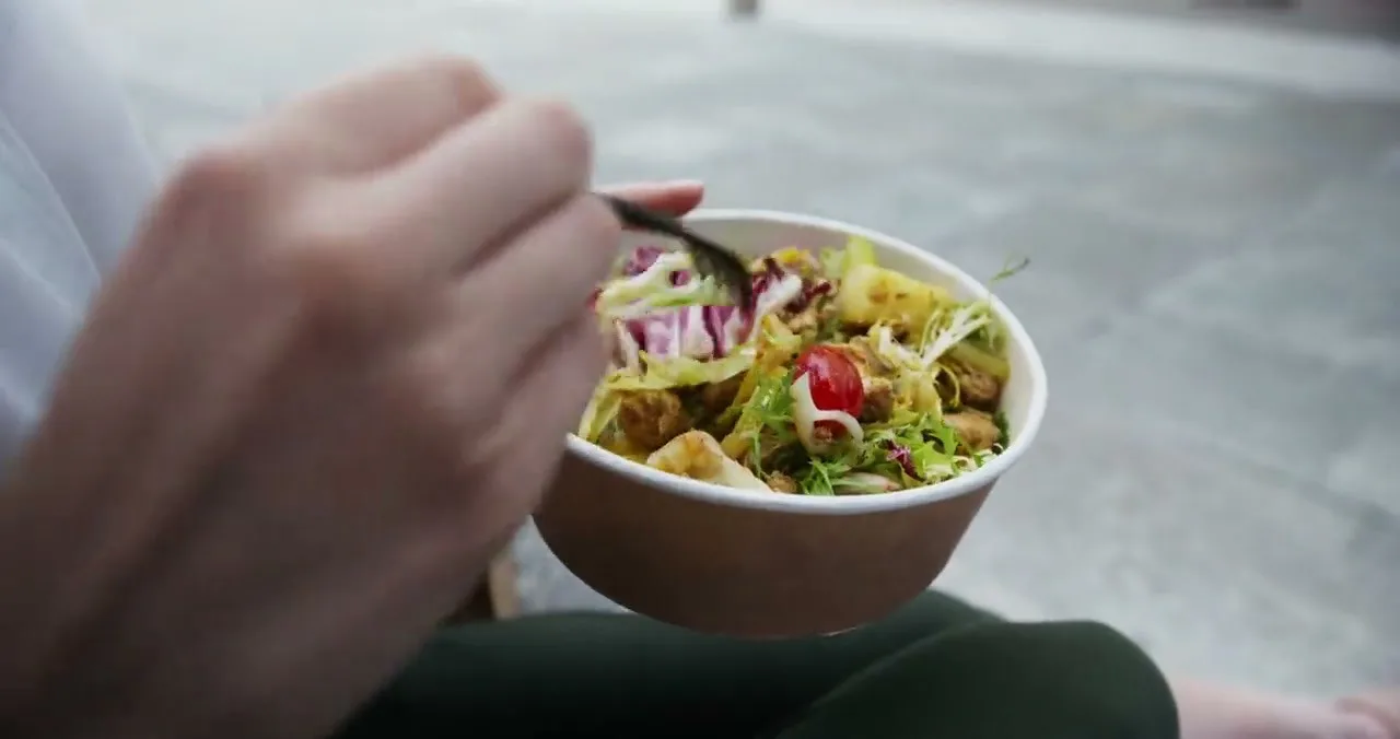 A hand holding a bowl of shredded salad and slaw